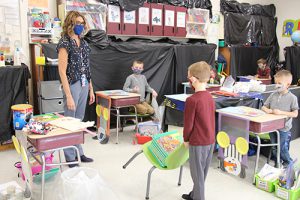 A teacher watches as a boy pulls a chair piled with books showing how easy it is to move things.