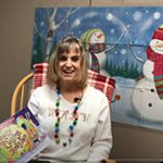 A woman sitting in a rocking chair wearing a Christmas sweater holds a book