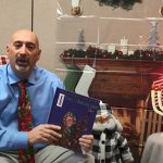 A man in a blue shirt and red holiday tie holds a book in f