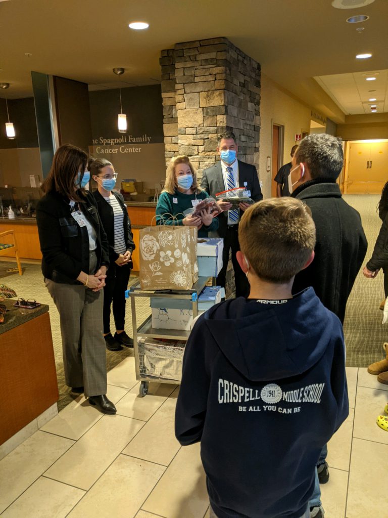 A young man wearing a blue Crispell Middle School hoodie is facing a group of seven adults who have shopping bags.