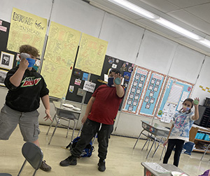 Three students hold the bowls they made. They all have masks on and are standing apart from each other.