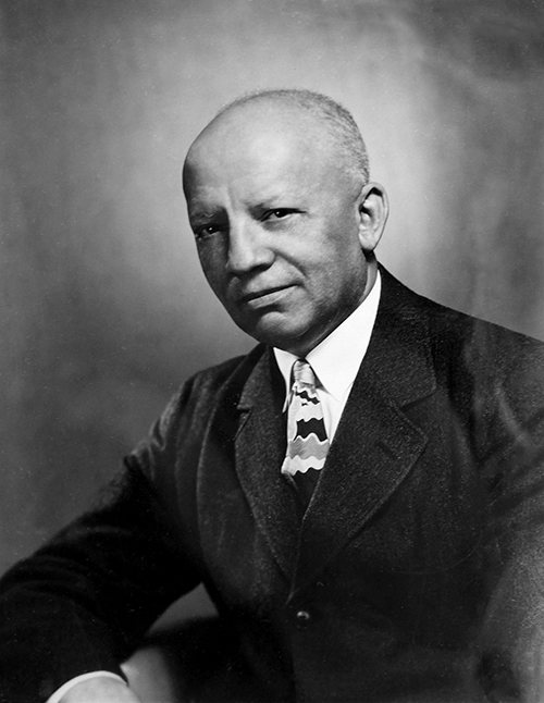 An old time photo in black and white of a man with a white shirt, striped tie and black suit jacket