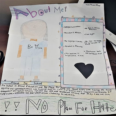 A sheet of paper with a girl drawn on one side and a listing of things about her on the left. It says No place for hate at the bottom.