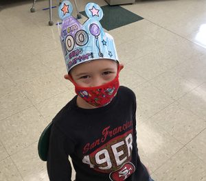 A boy in a black shirt wearing a red mask also has a hand-colored crown on saying I'm 100 days smarter.