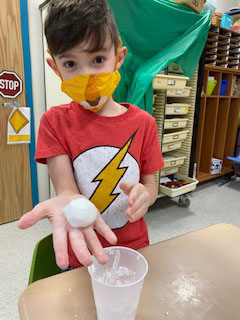 A little boy wearing a red shirt with the Flash logo. He is holding out his hand with a small snowball on it.
