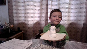 A boy wearing a green shirt holds a piece of paper that has a three-tiered snowman on it.