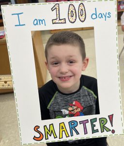 A smiling boy is in the center of an oversized photo frame that says I am 100 days Smarter!