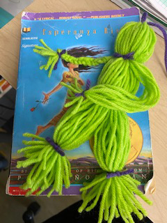 A green yarn doll sits on top of a book