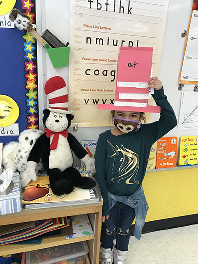 A girl wearing a dark shirt with a gold unicorn on it holds up a red and white paper hat.