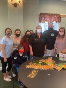 Eight people, both kids and adults, stand around a table with candy and bags on it.