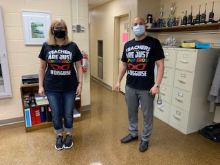 A woman on the left and a man on the right are both wearing facemasks and t shirts that say Teachers are just super heroes in disguise.