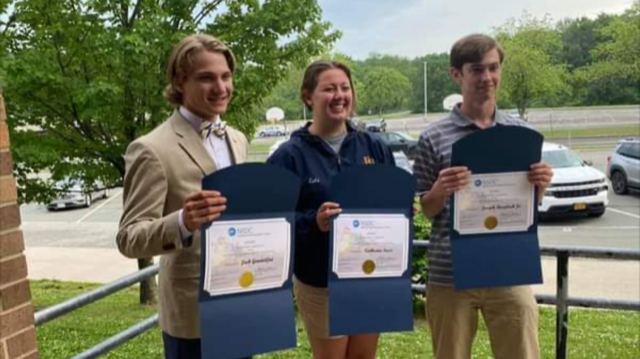 Three high school juniors stand holding certificates. The boy on the left is wearing a tan jacket, white shirt and tan bow tie; the girl in the center is wearing a blue jacket, her long hair is pulled back. The boy on the right is wearing a blue and gray shirt. All are smiling.