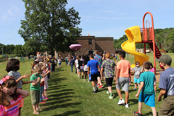 A line of fifth-grade students walk through the grass as two lines of younger kids clap for them as they pass.