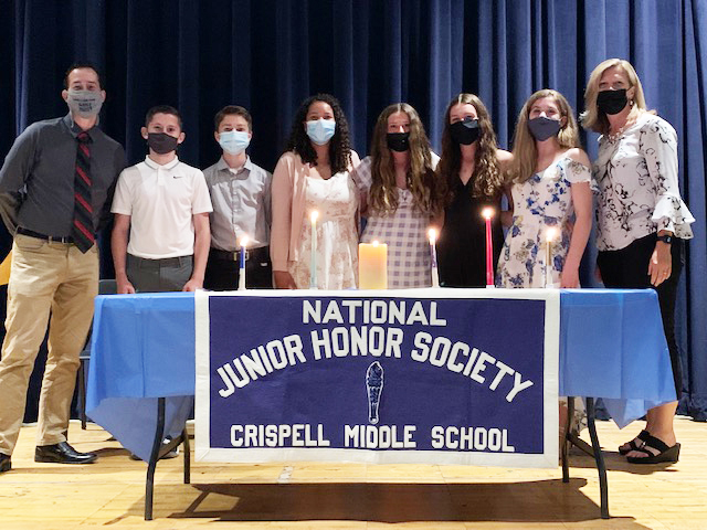 A table with five candles on it and a banner that reads National Junior Honor Societey Crispell Middle School. Behind it are two adults on either end and five students. All are wearing masks. 