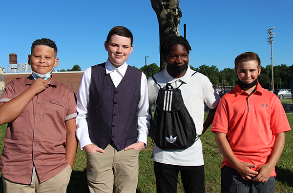 Four eighth-grade boys stand together, with a blue sky in the background. They are all dressed nicely.