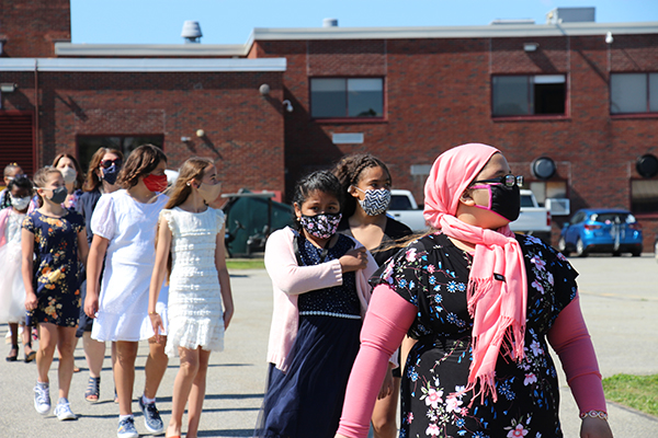 A group of fifth grade girls walk  in a single-file line. They are all wearing masks