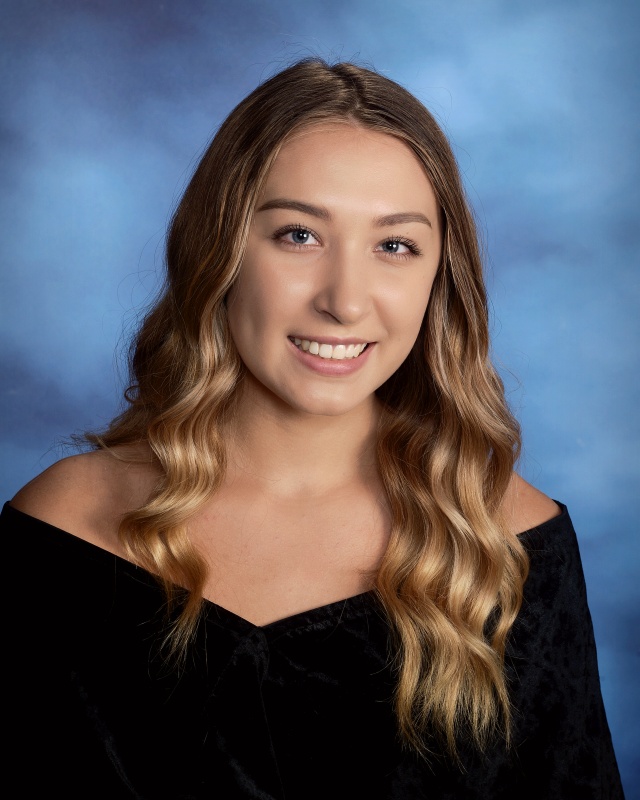 A high school age young woman in a formal graduation photo. She has long blonde hair and is wearing a black off-the-shoulder sheath. She is smiling.