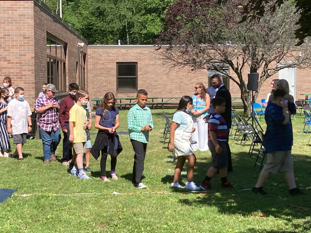 Elementary students dressed nicely walk in a line on grass.