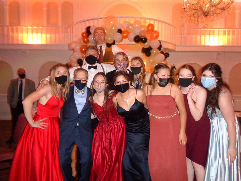 A large group of high school prom goers, in gowns and tuxedos.