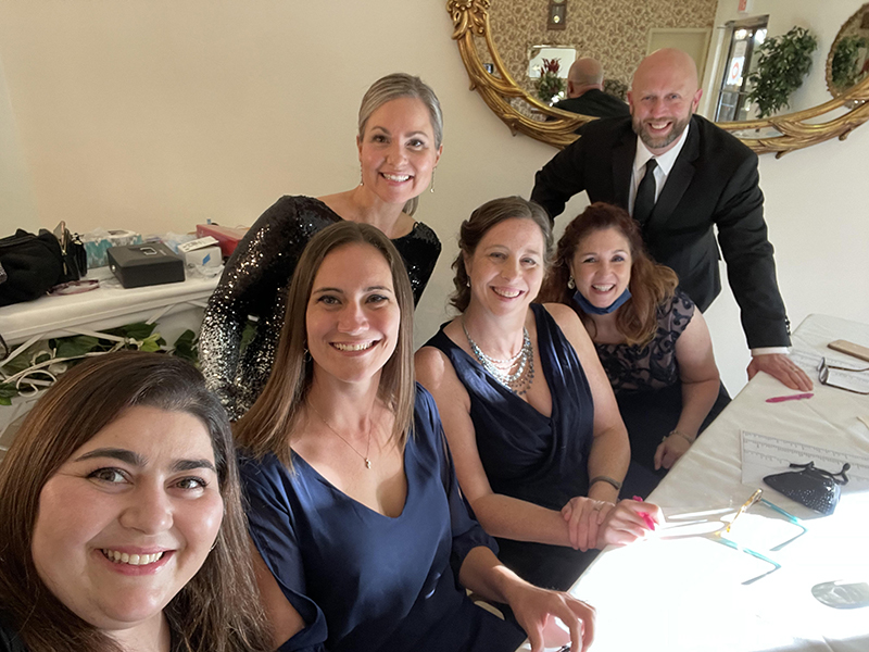 A group of six high school teachers, all dressed up, ,sit at a table at the prom.