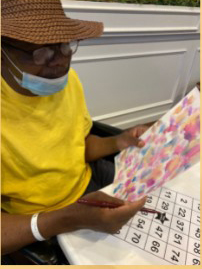 An older man in a yellow shirt and blue mask holds a piece of abstract artwork.