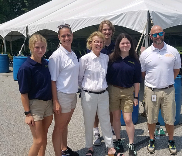 Six people standing together smiling. There is a tent in the background.