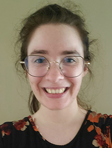 A young woman with wire rimmed glasses and long brown hair pulled back into a ponytail smiles. 