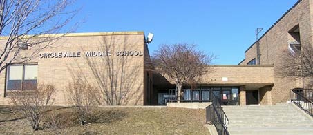 A tan brick building that says Circleville Middle School on it. On the right are stairs leading to the building. There are bare trees in front of it.