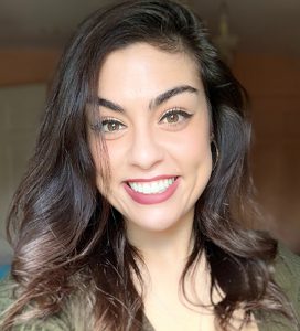 A woman with long wavy dark hair smiles broadly.