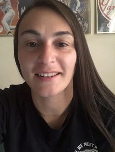 A young woman with long dark hair wearing a dark shirt smiles.