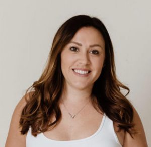 A woman with a big smile, long brown hair and a white tank top.