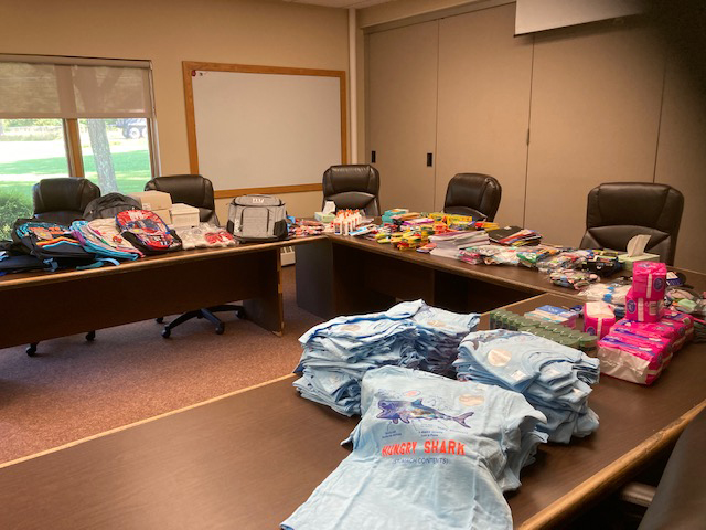 Three large tables in the shape of a  U-shaped table are filled with schools supplies. 