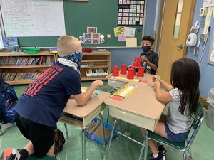 Three students sit at three desks. They are all holding strings to move the cups into position.