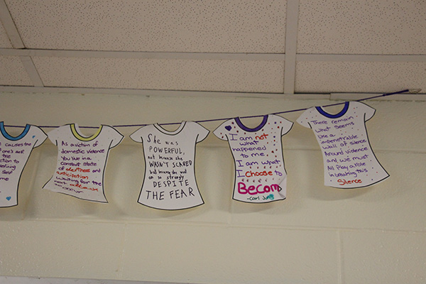 A clothesline with paper shirts on it. The shirts all have empowering messages about domestic violence survivors.