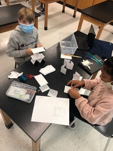 A sixth-grade boy and girl sit at a lab table building towers out of index cards.