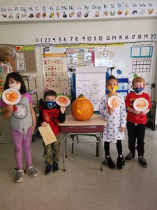 Four kindergarten students hold plates that have been made into pumpkins. In the center of them is a jack-o-lantern.
