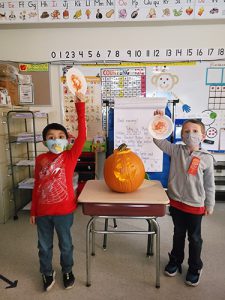 Two boys hold up high their plates that they've made into pumpkins. Between them is a jack-o-lantern.