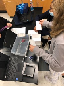 A sixth-grade girl with long blonde hair builds a tower of index cards on a black lab table.