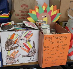 Large cardboard boxes decorated for Thanksgiving. One had several turkeys traced from hands and colored brown yellow and orange. The other has a construction paper turke on the back and a sign on the front that says Happy Thanksgiving from Room 228 with a list of names on it.