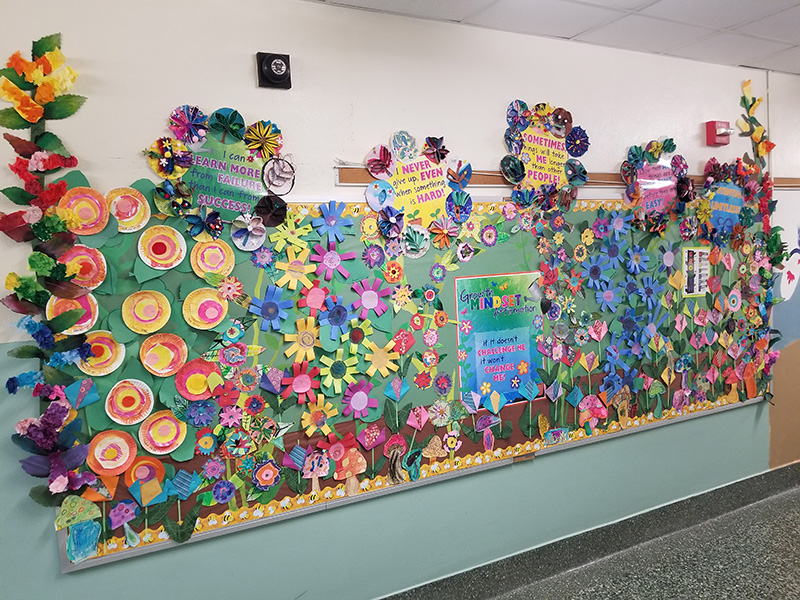 A long bulleting board covered in multi-colored paper flowers. There are positive messages along the flowers.