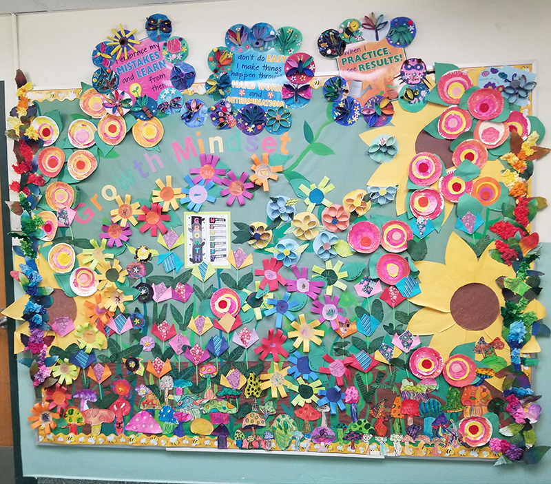 A bulletin board of many multi-colored paper flowers.