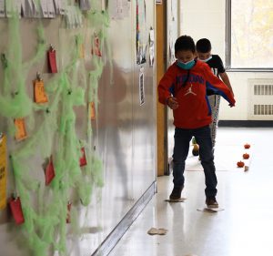 An elementary boy stands on pieces of paper on the floor, as he leaps from one to the next.
