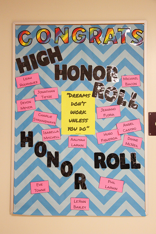 A bulletin board that says High Honor Roll, Honor Roll. There are pine pieces of paper around it with names on it and a yellow piece in the center that says Dreams Don't Work  Unless You Do.