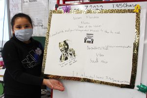 A third grade girl holding a poster with pictures of Nelson Mandela on it.