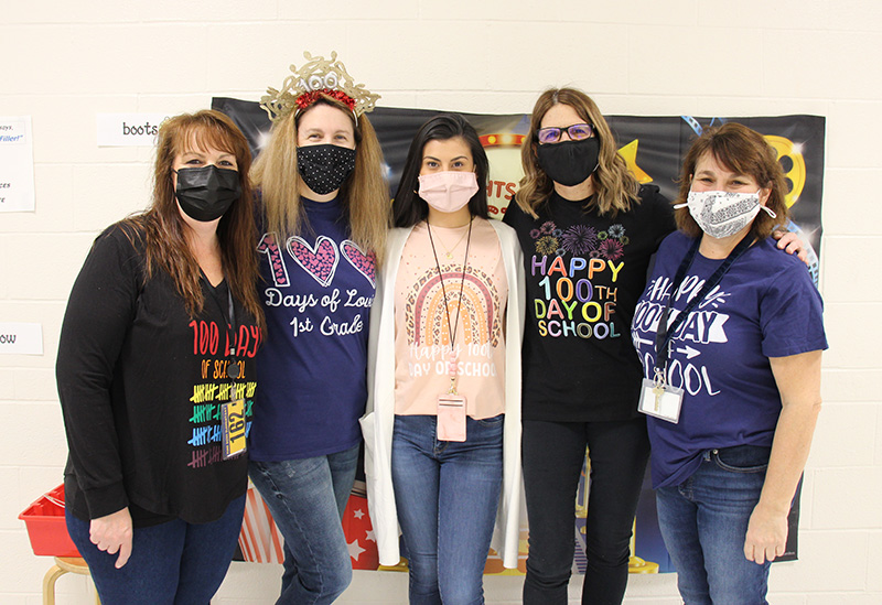 Five women stand together, all wearing shirts that mark the 100th day of school.