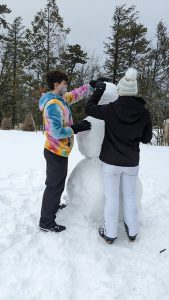 Two high school students build a large snowman.