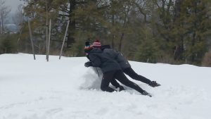 Two high school students push a large boulder of snow as they make a snowman.