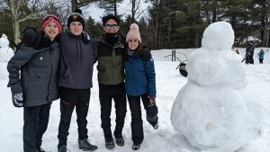 Three high school students stand next to a large snowman.