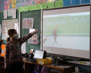 A third grade girl points to a screen. On the screen is a gymnast and the name Simone Biles.