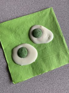 A green napkin with two cookies on it that look like green eggs.